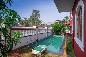 A swimming pool with a tiled deck, surrounded by a white wall with red accents and a glass balustrade. - Casa Riana (Alto de Porvorim)