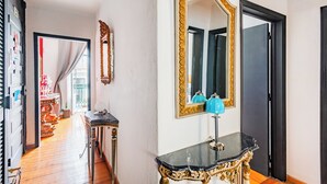 A hallway with a black and gold console table, a large ornate mirror, and a door with a black frame.