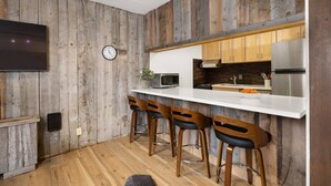 Une cuisine avec des murs en bois, un plan de travail blanc et des tabourets de bar.
