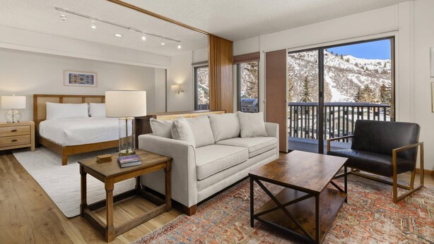 Une chambre d’hôtel moderne dotée d’une grande fenêtre donnant sur les montagnes, d’un lit confortable, d’un canapé, d’une table basse et d’un fauteuil.