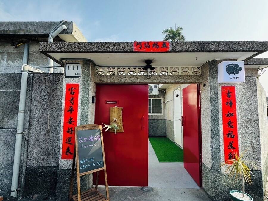 Une entrée d’immeuble avec une porte rouge, une enseigne et deux banderoles verticales ornées de caractères chinois.