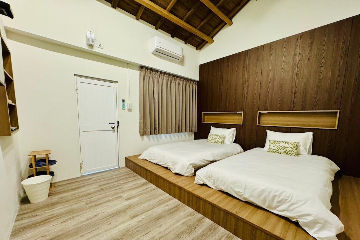 A bedroom with two beds, a wooden headboard, a white door, and an air conditioning unit.