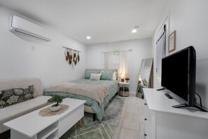A modern bedroom with a bed, a sofa, a TV, and an air conditioner. - Cozy studio in Downtown Austin! (Austin)
