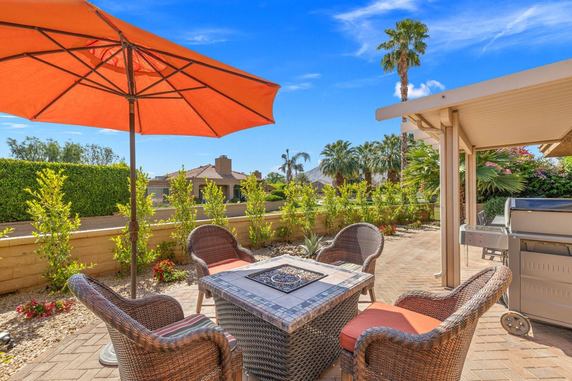 An outdoor patio with wicker furniture, a grill, and an orange umbrella.