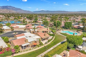 A residential area with houses, a swimming pool, and a mountain range in the background. - Oasis in Hidden Palms! Pool, Spa, Pickle Ball, Gated Community (Palm Desert)
