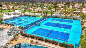 A large outdoor tennis court complex with multiple courts, surrounded by residential buildings and palm trees. - Oasis in Hidden Palms! Pool, Spa, Pickle Ball, Gated Community (Palm Desert)