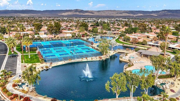 A large outdoor swimming pool with multiple lanes, surrounded by palm trees and a fountain. - Oasis in Hidden Palms! Pool, Spa, Pickle Ball, Gated Community (Palm Desert)