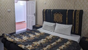 Habitación de hotel con cama, mesita de noche, una puerta blanca y equipo de aire acondicionado en la pared.