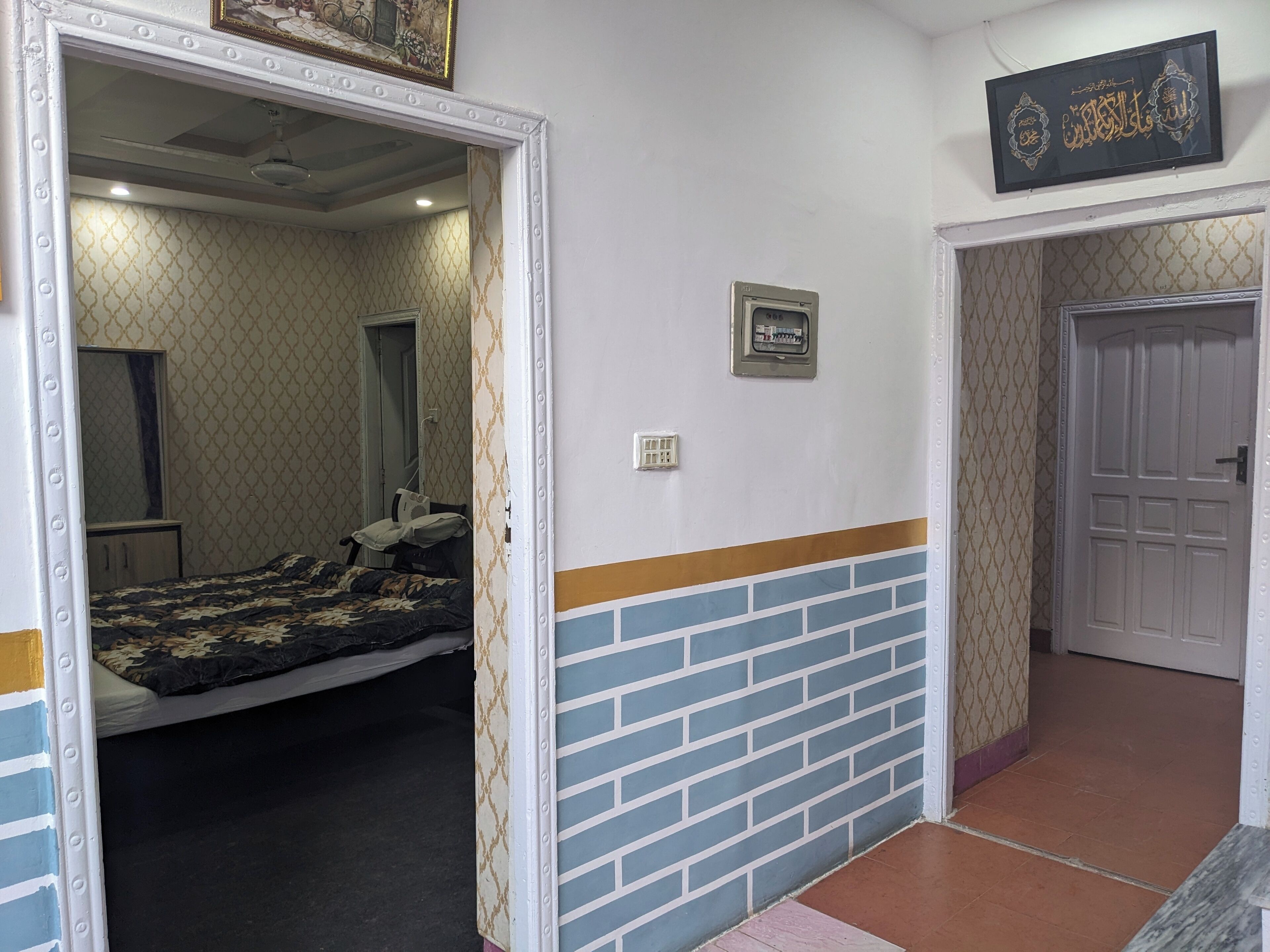 A room with a bed, a mirror, a door, and a wall-mounted electrical outlet.