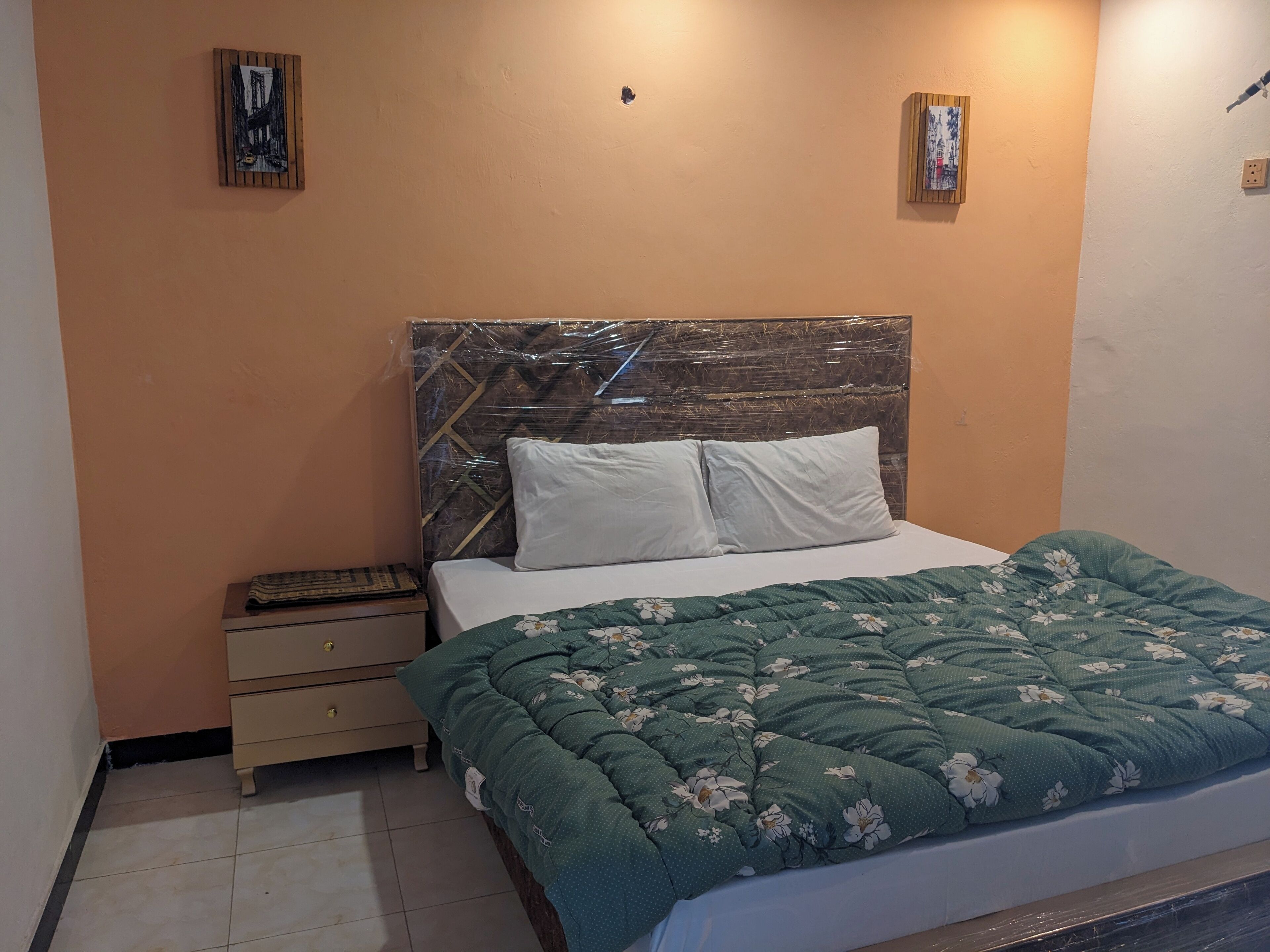 A bedroom with a bed, a nightstand, a dresser, and two wall-mounted artworks.