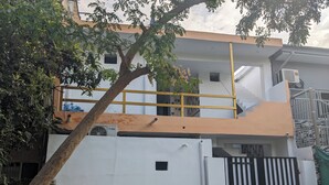 Un edificio de varios pisos con fachada blanca, barandilla amarilla en el nivel superior y entrada protegida por una reja.