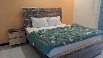 A neatly made bed with a green floral bedspread, a wooden headboard, and white pillows.