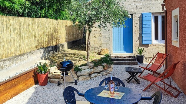 Eine Terrasse im Freien mit einem runden Tisch, Stühlen, einem Grill und einer blauen Tür.