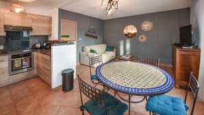 Eine moderne Küche mit Einbauofen, ein Essbereich mit einem Mosaik-Tisch und ein Wohnbereich mit Sofa und Wandbildern.