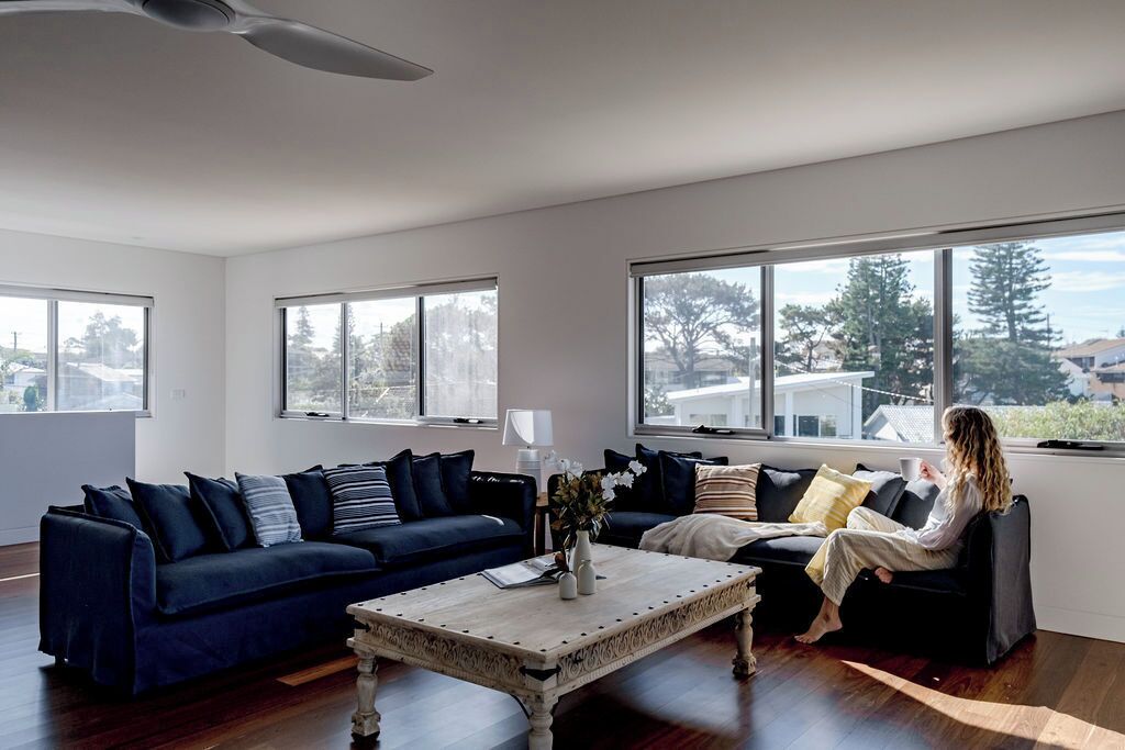 A modern living room with a dark blue sofa, a white coffee table, and a person sitting on a black sofa.