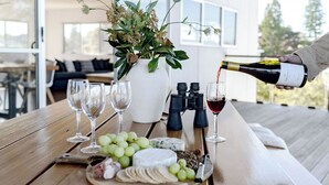 Una mesa de madera con una tabla de quesos, uvas y una botella de vino sirviéndose en una copa.