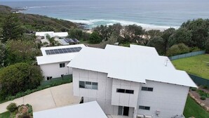 Una casa moderna de dos pisos con techo plano, paneles solares y vista al océano.
