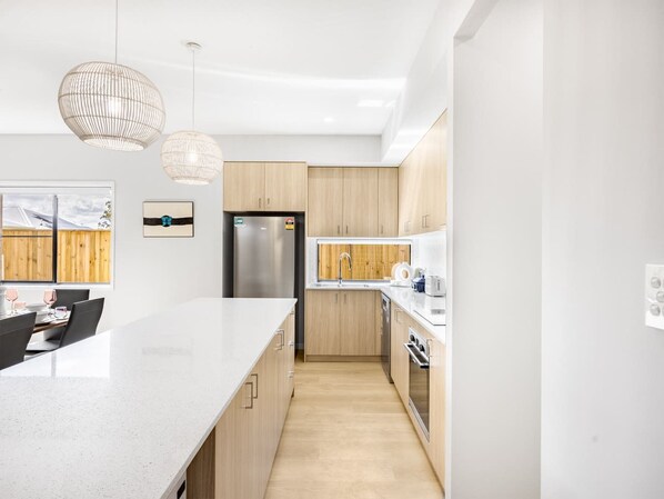 A modern kitchen with a large island, stainless steel appliances, and light wood cabinetry.