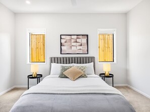 A bedroom with a bed, two bedside tables, a headboard, and two wall-mounted picture frames.