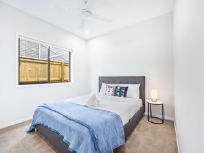 Un dormitori amb un llit, una finestra amb vistes, un ventilador de sostre i una taula de nit amb una làmpada.