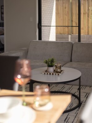 A modern living room with a grey sofa, a round coffee table with decorative items, and a glass of wine.