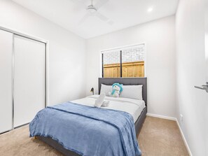 A bedroom with a bed, a ceiling fan, a window with a brick pattern, and a door.