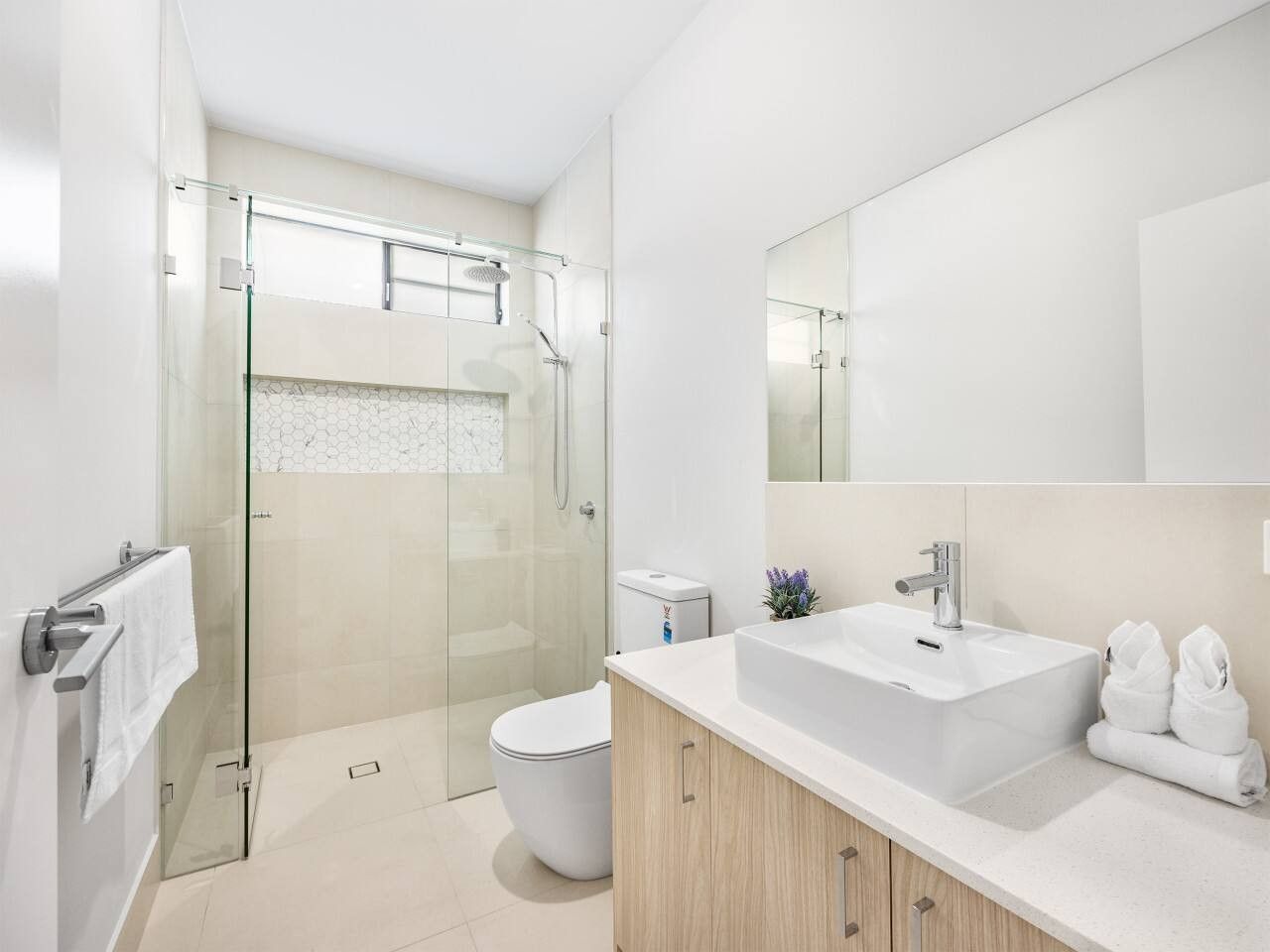 Une salle de bain moderne avec une douche à parois de verre, un lavabo blanc et un grand miroir.