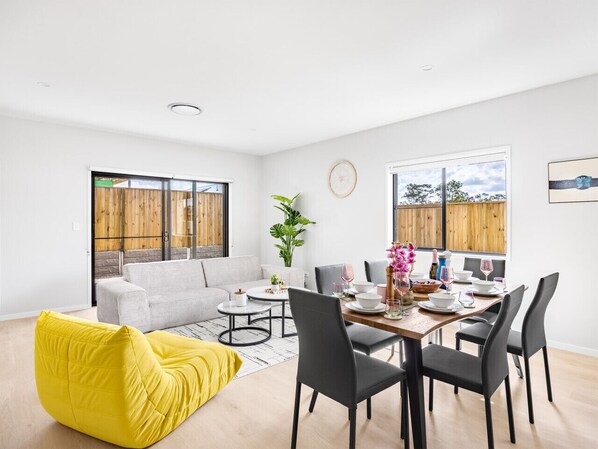A modern living room with a dining area, a yellow bean bag, a grey sofa, and a dining table set for four.