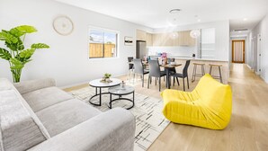 A modern living room with a grey sofa, a yellow bean bag, and a dining area with a kitchen in the background.