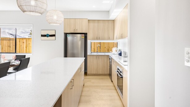 A modern kitchen with a large island, wooden cabinets, stainless steel appliances, and pendant lighting.
