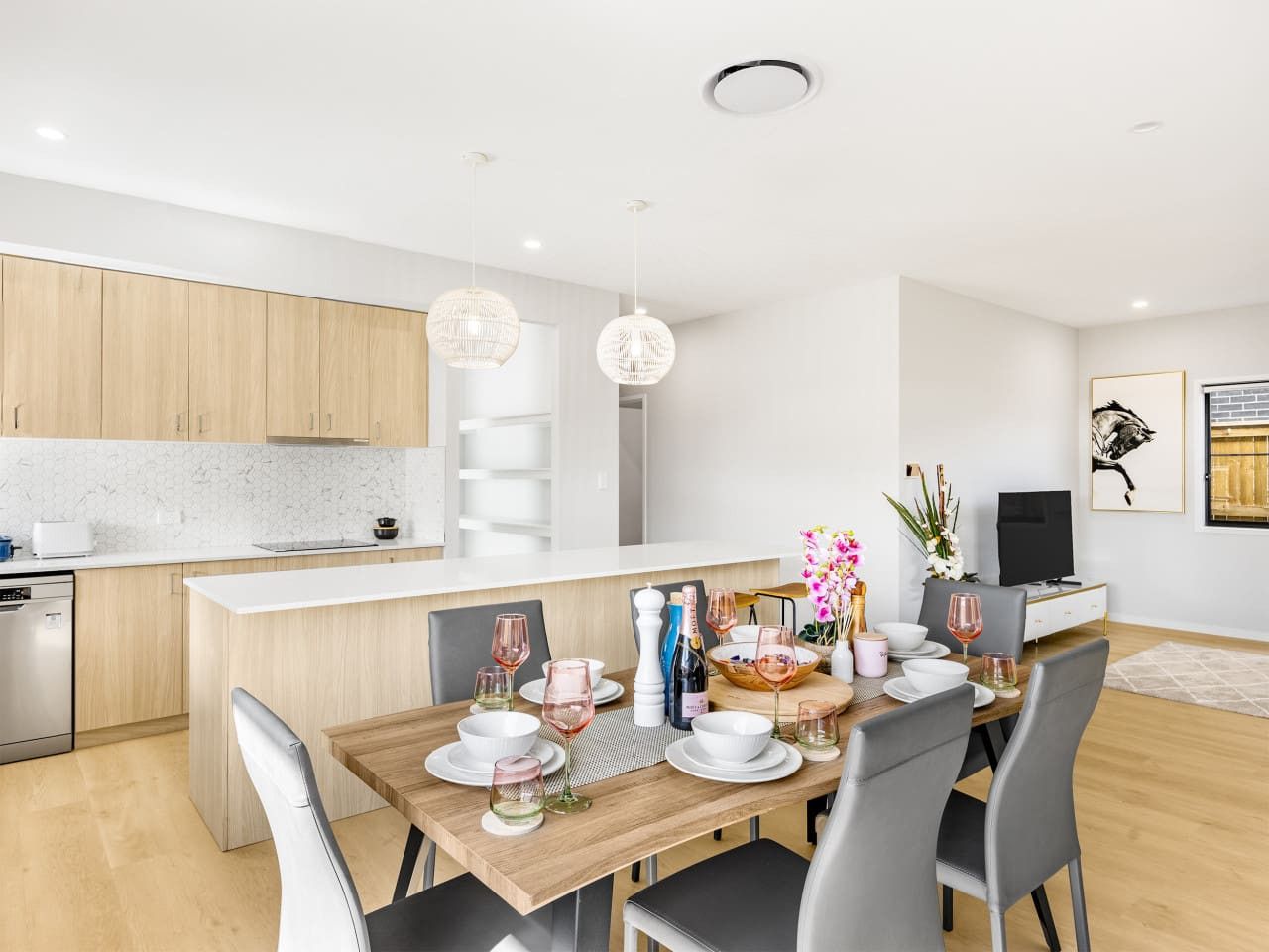 A modern kitchen with a dining area, wooden cabinets, and a TV.
