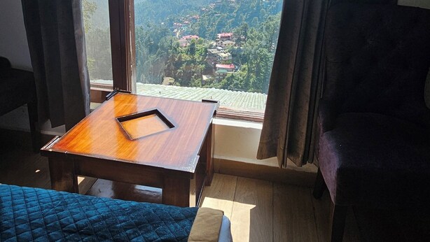 Una stanza con un letto, un tavolo di legno e vista su un paesaggio montuoso attraverso ampie finestre.