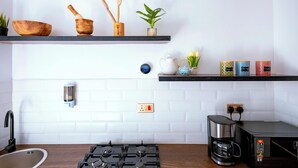 Een moderne keuken met een gasfornuis, een koffiezetapparaat en een magnetron. Op een plank staan houten kommen en keukengerei, en er staat een potplant.