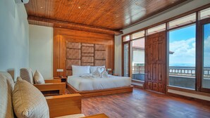 A spacious bedroom with a large bed, wooden headboard, and a view of the sea through large windows. - Alpine Holiday Inn, Kufri, Shimla (Theog)