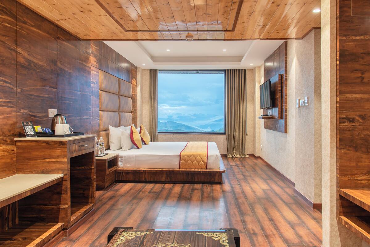 A modern hotel room with a large bed, wooden flooring, a desk, and a TV mounted on the wall.