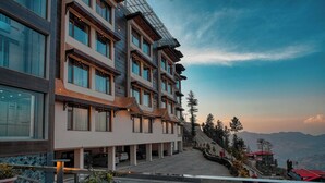 A multi-story hotel with a modern design, featuring large windows and a covered outdoor area with potted plants. - Alpine Holiday Inn, Kufri, Shimla (Theog)