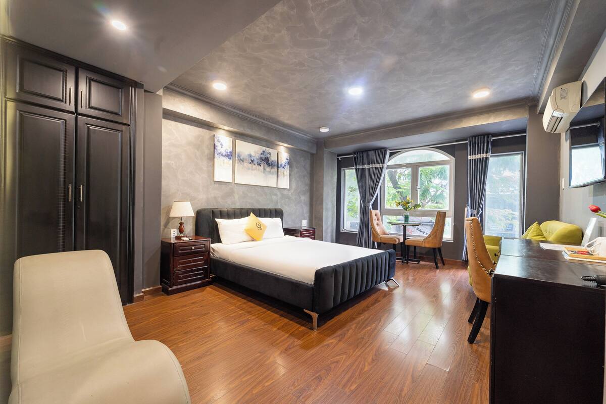 A modern hotel room with a large bed, a desk, a chair, and a view of the outdoors.
