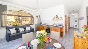 Un appartement moderne comprenant un salon, une cuisine et un coin repas. Il est doté d’une grande fenêtre, d’un canapé, d’une table à manger avec des chaises et d’appareils électroménagers.