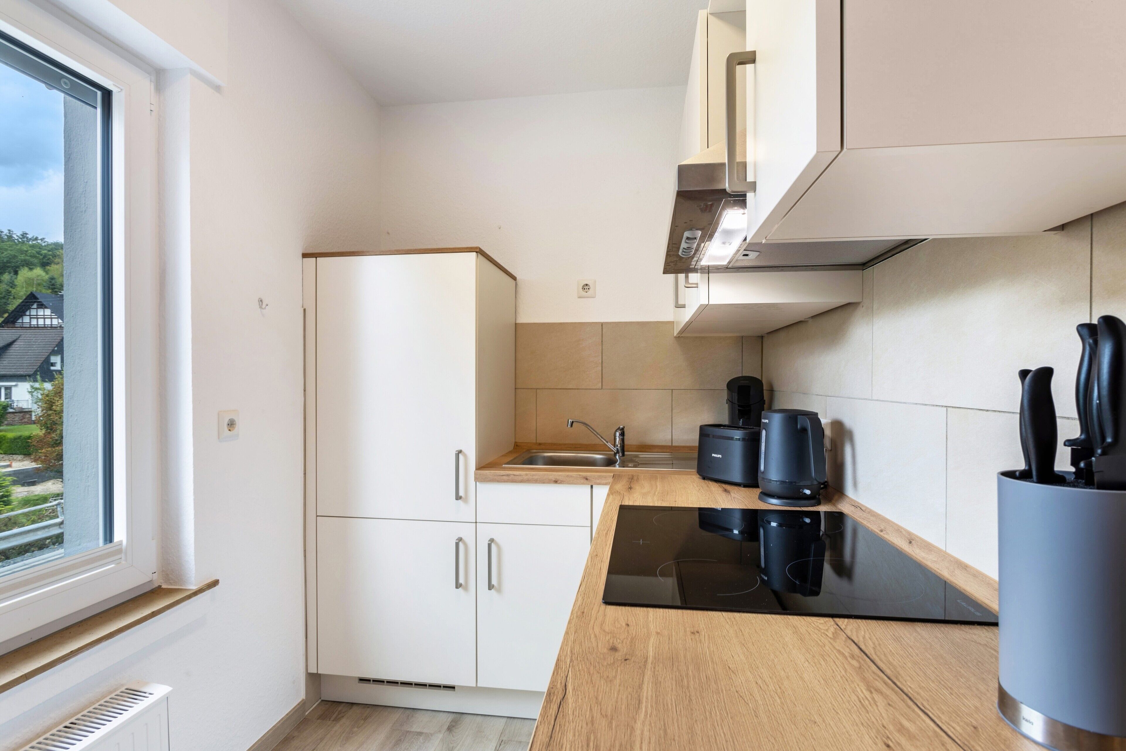 A modern kitchen with white cabinets, a black countertop, and a window with a view of houses.