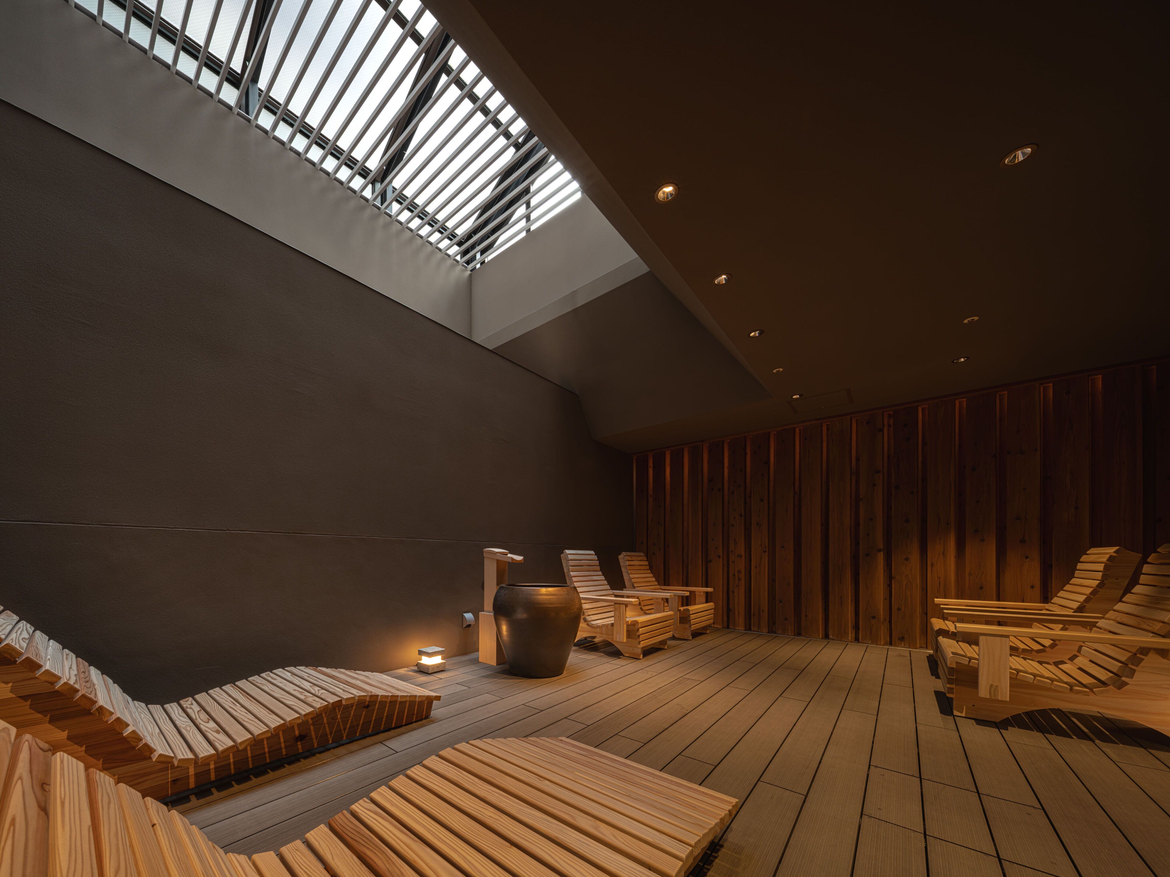 A spa area with wooden benches, a large vase, and a skylight.