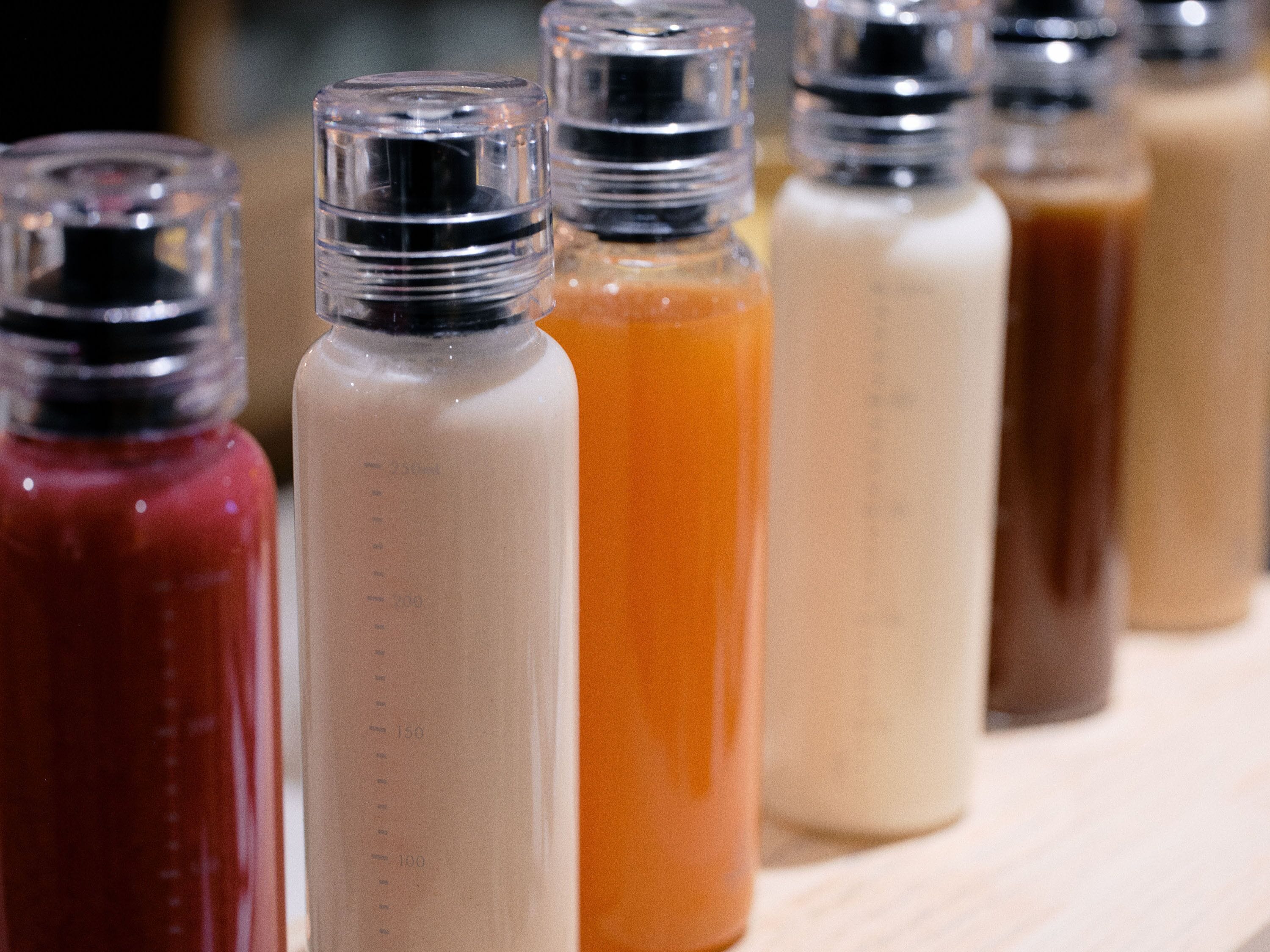 A row of clear glass bottles with measurement markings, containing different colored liquids.