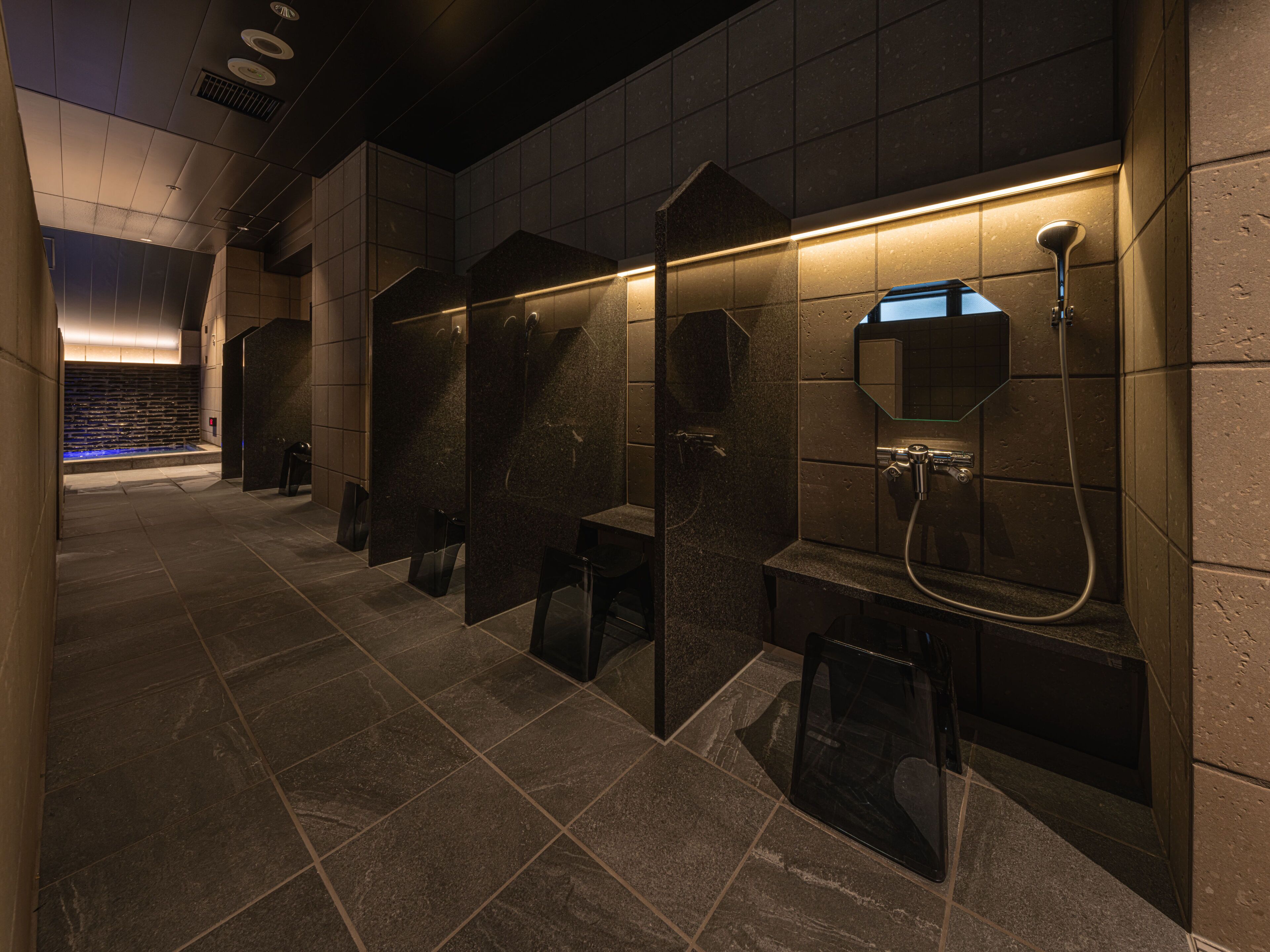 A modern bathroom with dark stone tiles, individual shower stalls, and a glass partition wall.