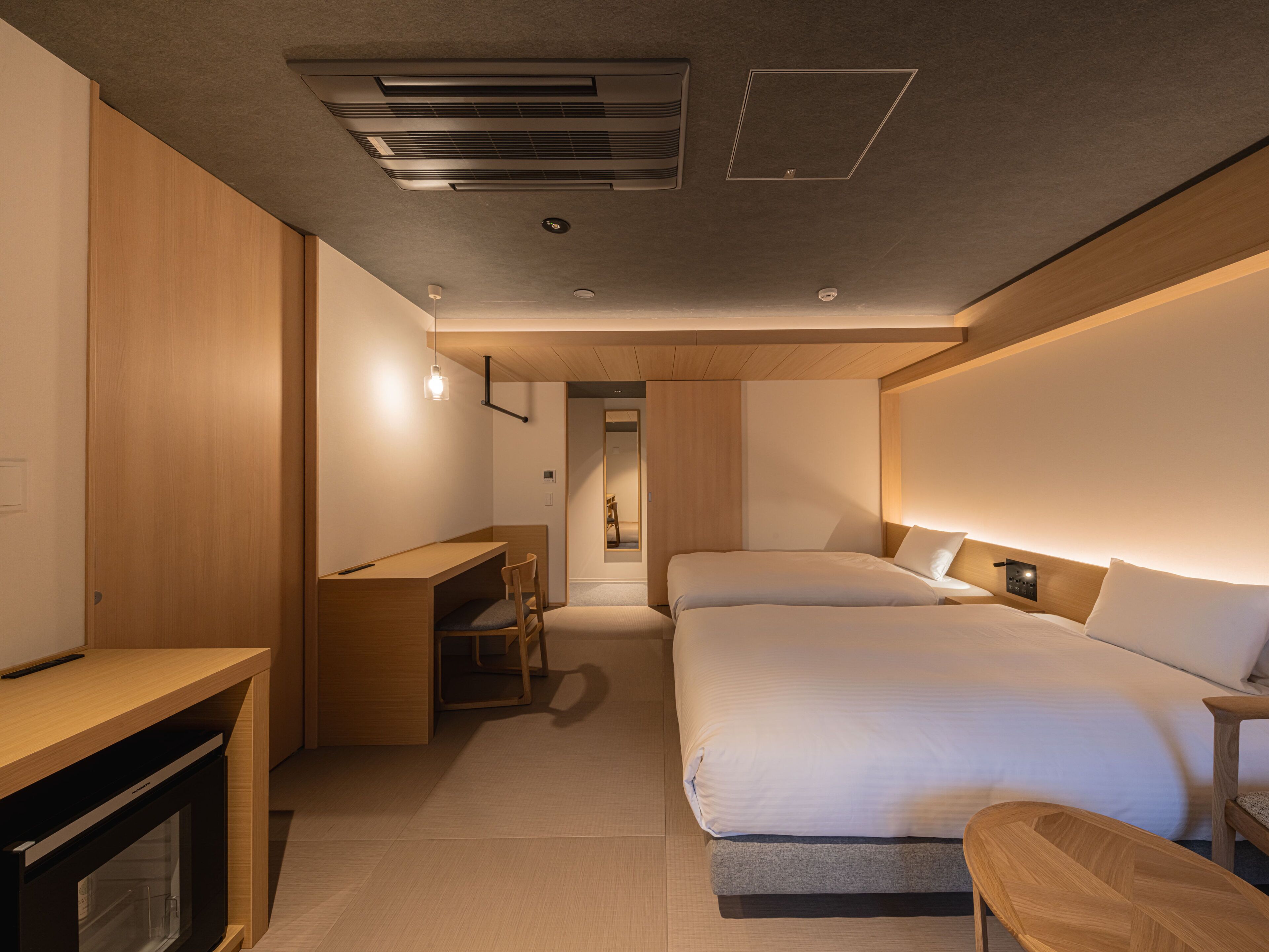 A modern hotel room with a bed, bedside table, desk, and a small seating area.