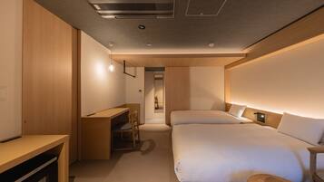 A modern hotel room with a bed, bedside table, desk, and a small seating area.