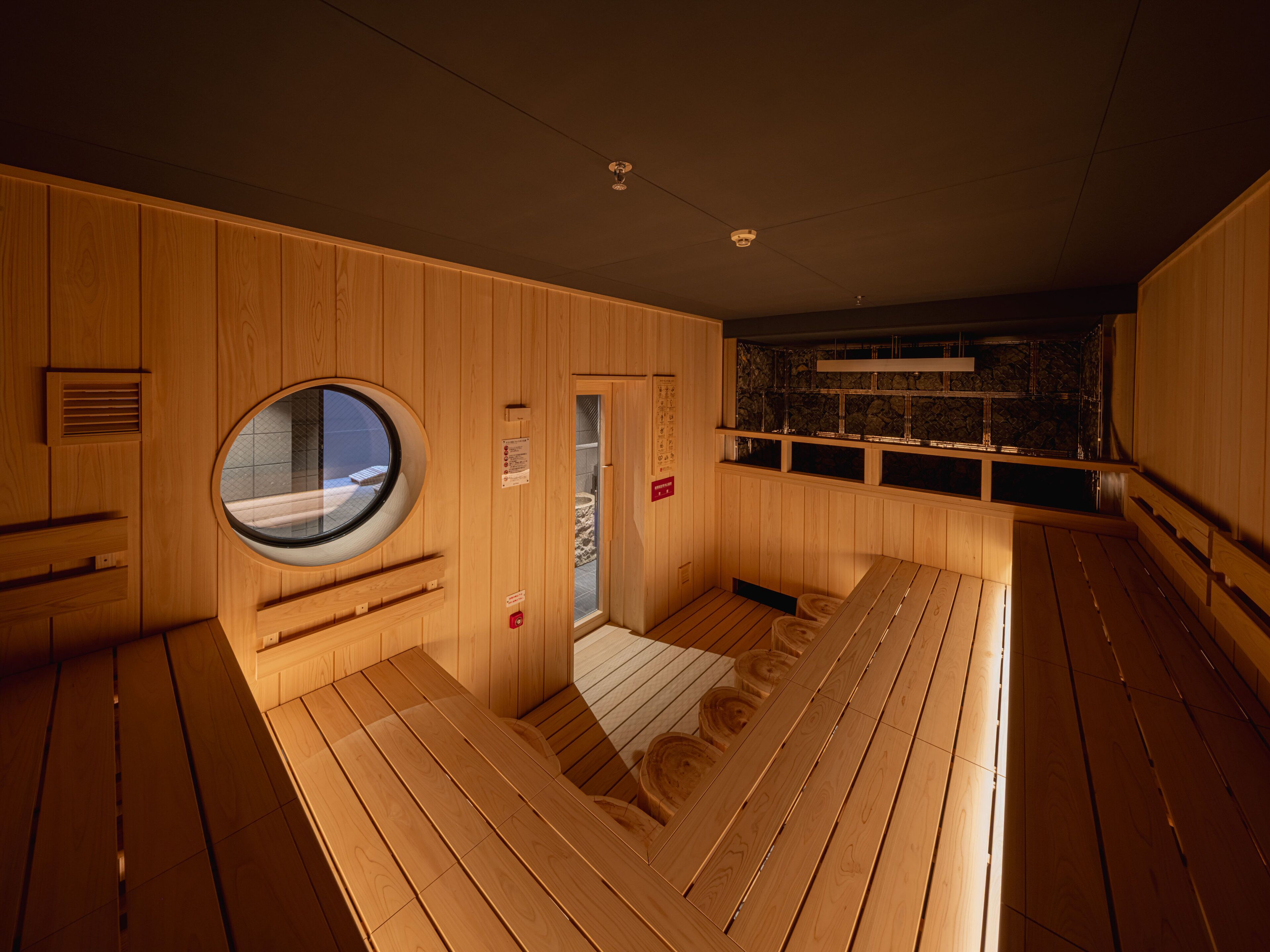 A sauna with wooden walls, a circular window, and a stone wall in the background.