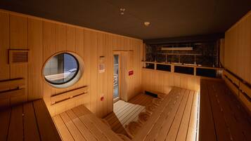 A sauna with wooden walls, a circular window, and a stone wall in the background.