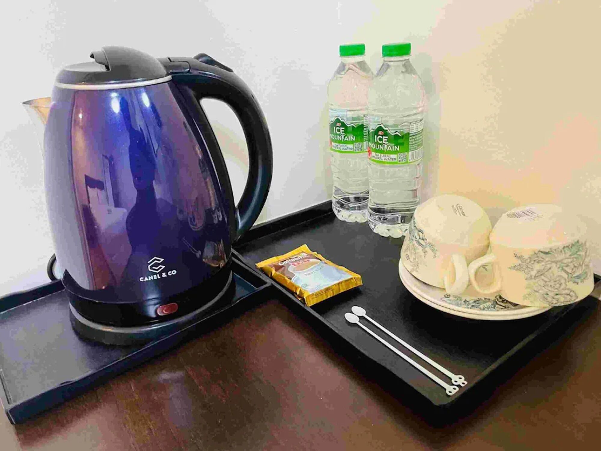 A tray with a blue electric kettle, two bottles of water, a packet of tea, and two teacups.