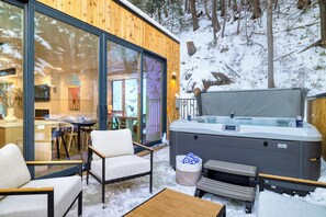 Un espace extérieur accueillant avec un coin salon, un jacuzzi, une terrasse en bois et des portes vitrées donnant accès à un espace intérieur.