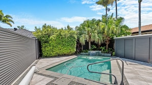 A swimming pool with a metal ladder, surrounded by a tiled patio and palm trees. - Spacious 4BR Poolside Escape (Burleigh Waters)