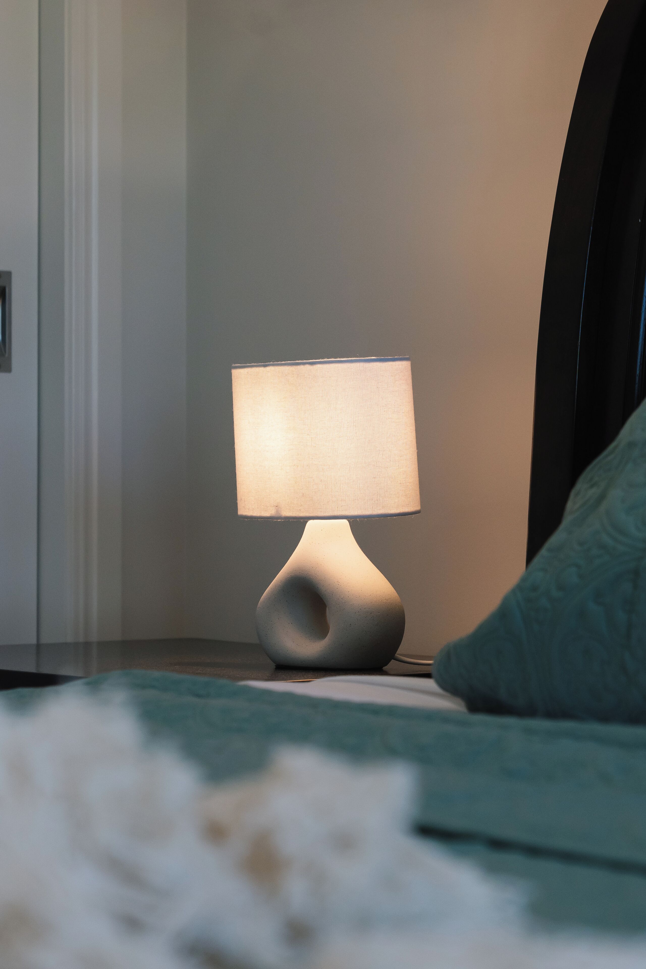 Een modern nachtkastje met een lamp, een groen kussen en een witte, gestructureerde deken.